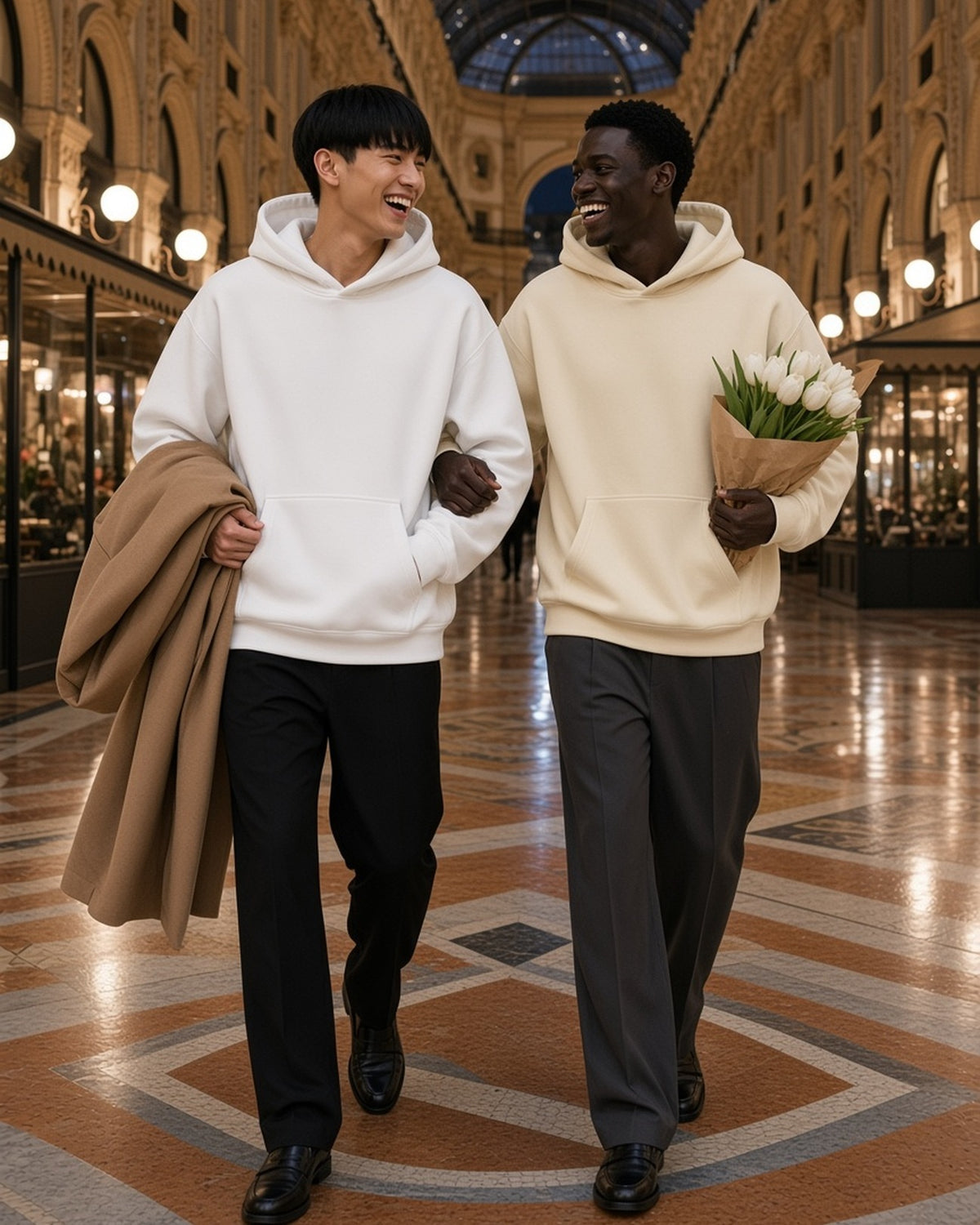 Two men in the Oversize Heavyweight Fleece Hoodie in Lucent White and Bone, arm in arm with white tulips in a Milan arcade at night