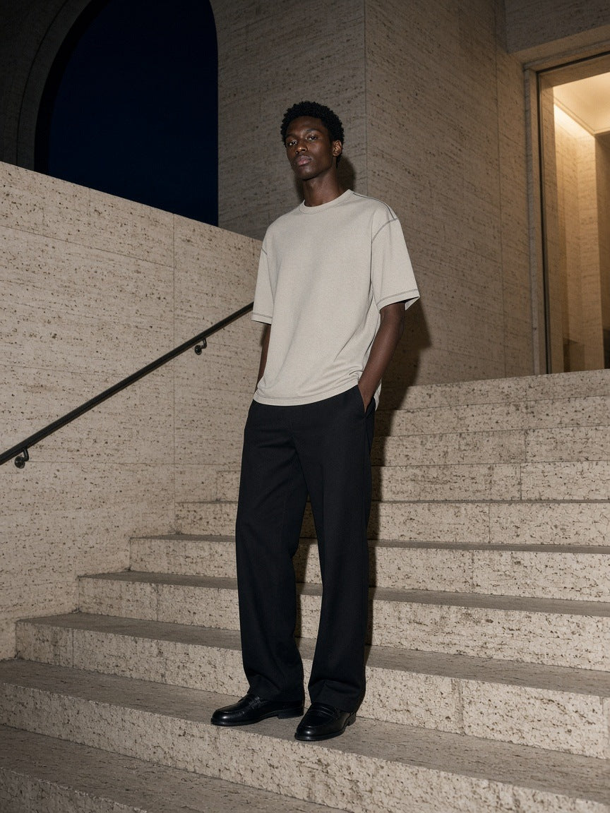 Marcel Afters Oversized Contrast-Stitched Cotton Tee in Beige, worn by a man, stone stairs