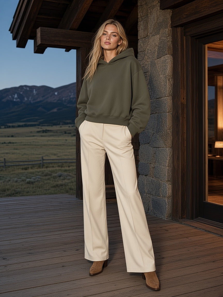 Marcel Afters Oversized Drop Shoulder Hoodie in Army Green, worn by a woman, standing on a timber deck at dusk in wide cream trousers