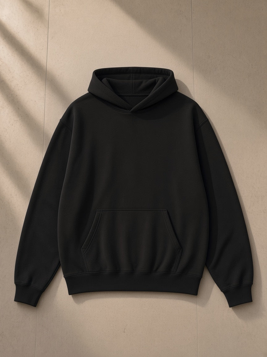 Unisex oversized heavyweight hoodie in Black, laid flat on pale limestone, front view