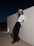 Marcel Afters Oversized One-Piece Boxy T-Shirt in White, worn by a woman, leaning on a wall under a desert night sky in a wide-brim hat