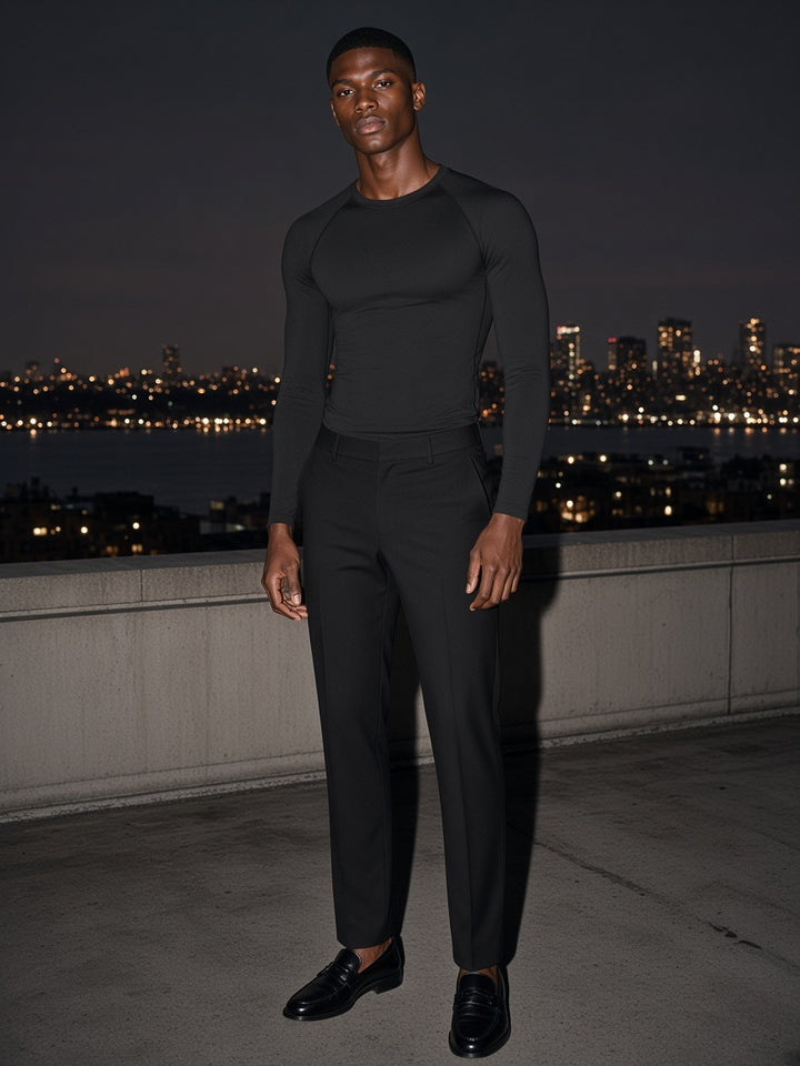 Man in the Performance Long Sleeve T-Shirt in Black, standing on a rooftop overlooking the city skyline at night