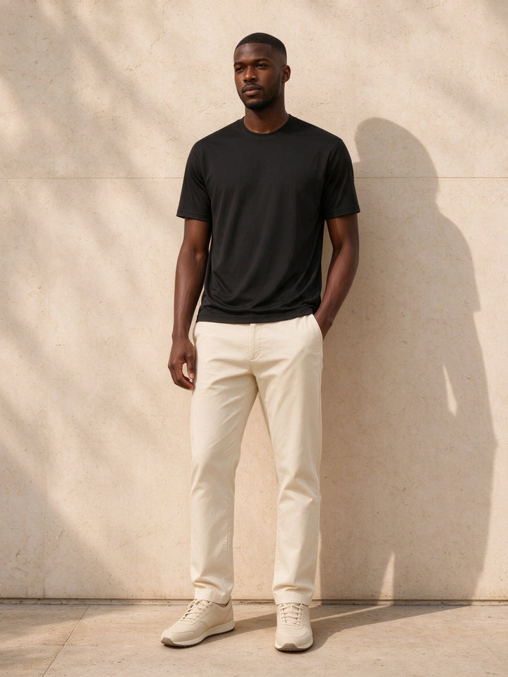 Marcel Afters Performance Short Sleeve T-Shirt in Black, worn by a man against a pale limestone wall with cream trousers and cream trainers