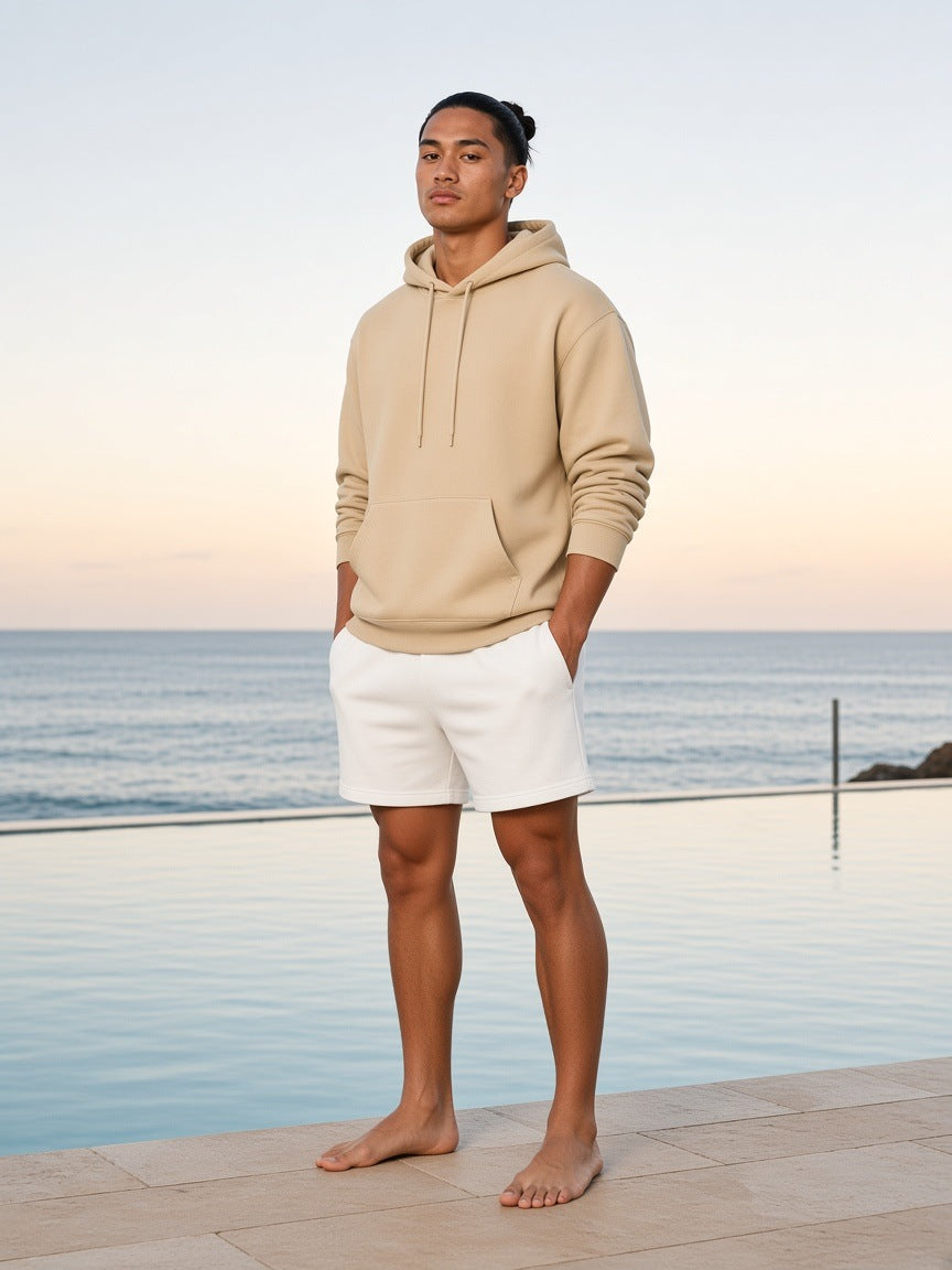 Marcel Afters Relaxed Pullover Hoodie in Khaki, worn by a man, standing barefoot on a pool terrace by the sea at sunset