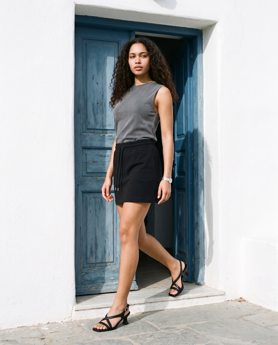 Woman in Gray reverse washed tank top and a black skirt at a blue door