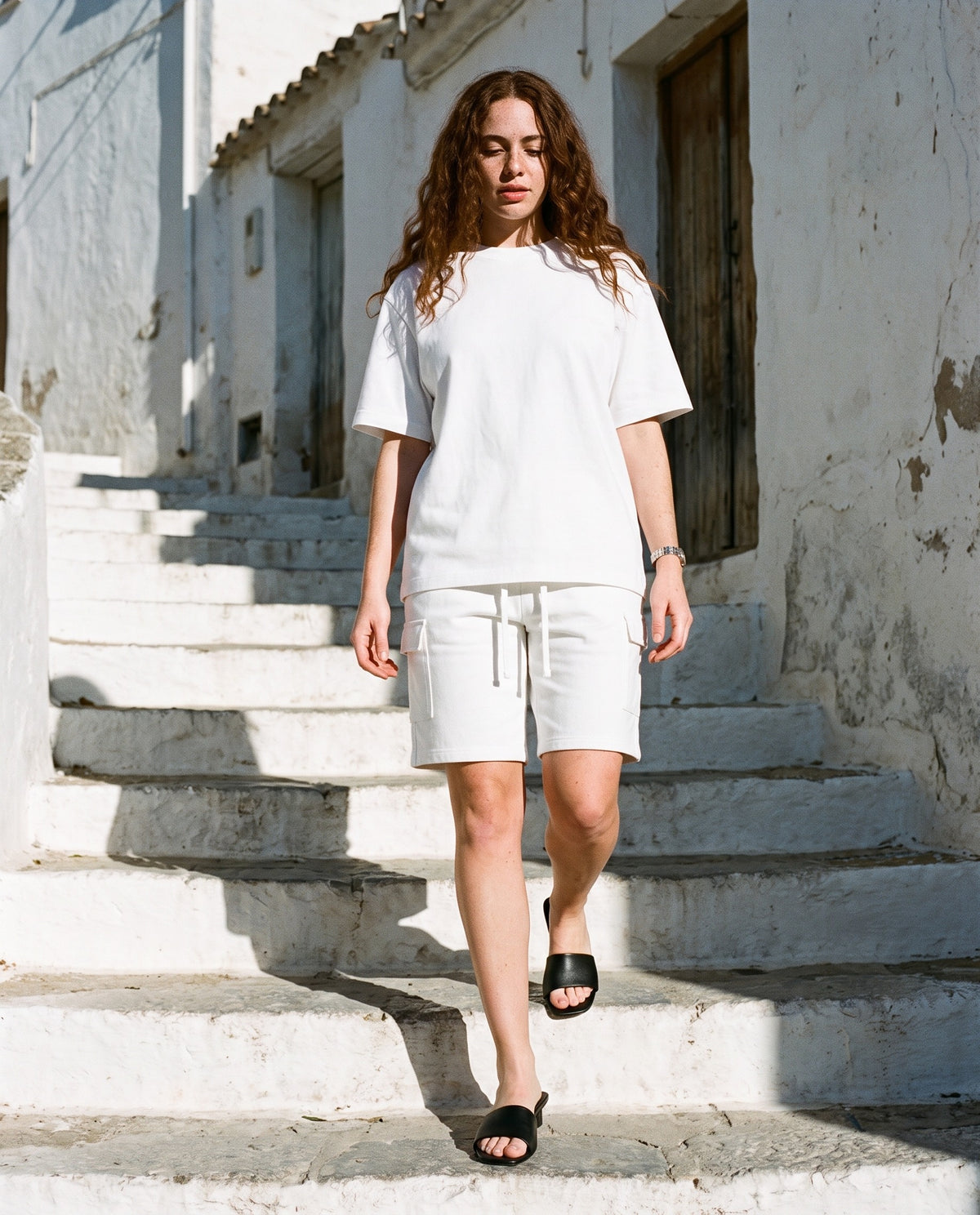 Woman wearing The Room Service Slide with the Oversized T-Shirt in White, Drawstring Cargo Shorts in White. Travel Light, Autumn–Winter 2026 campaign