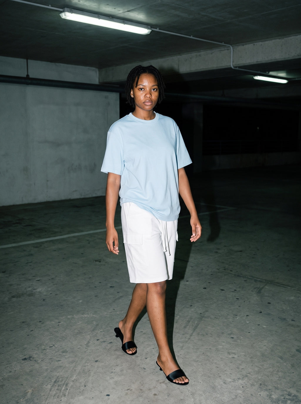 Woman wearing The Room Service Slide in Black with white drawstring cargo shorts and a sky blue oversized tee, flash photograph