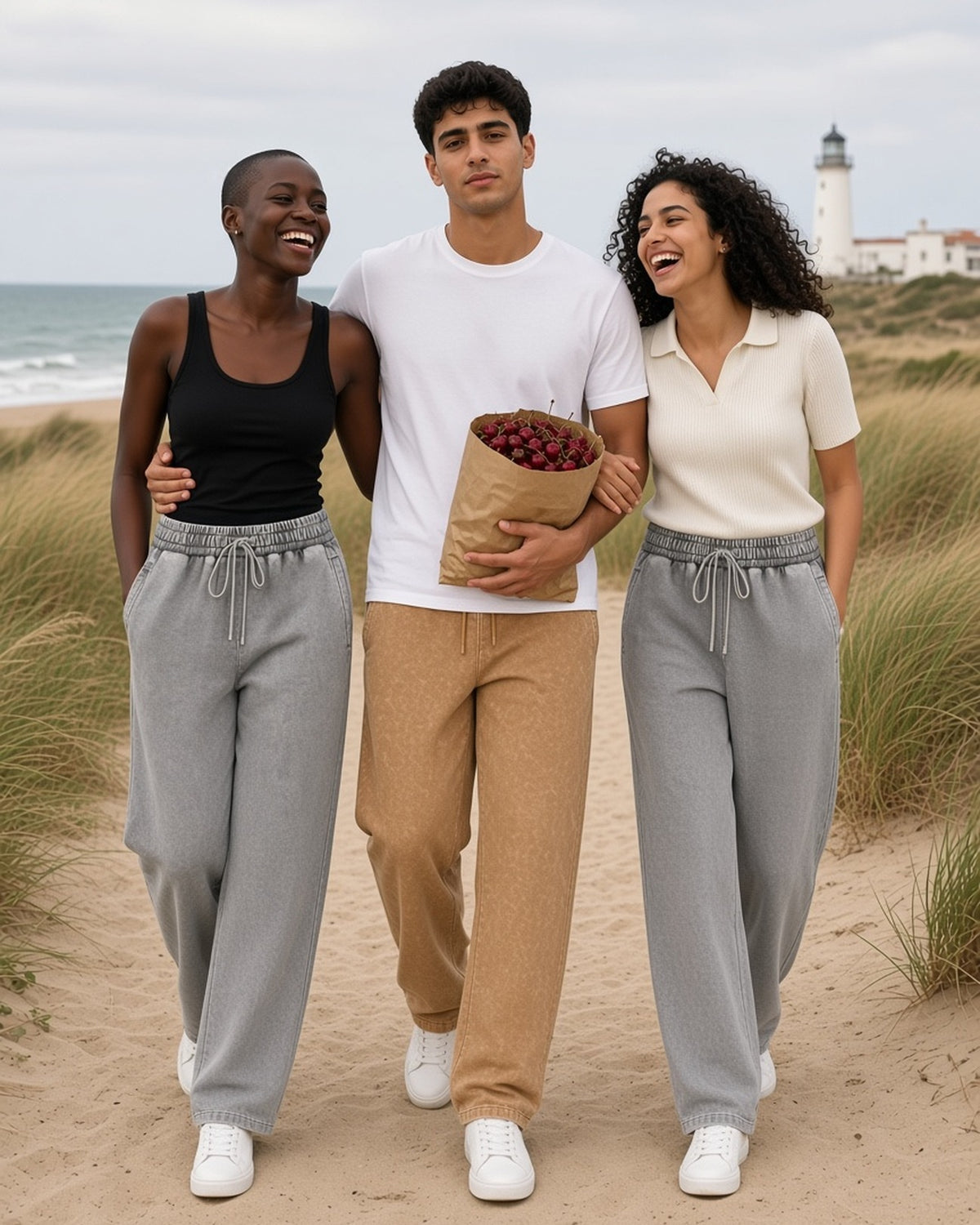 Three people in the Snow Wash Heavyweight Sweatpants in Light Gray and Brown, walking a coastal dune path with a bag of cherries