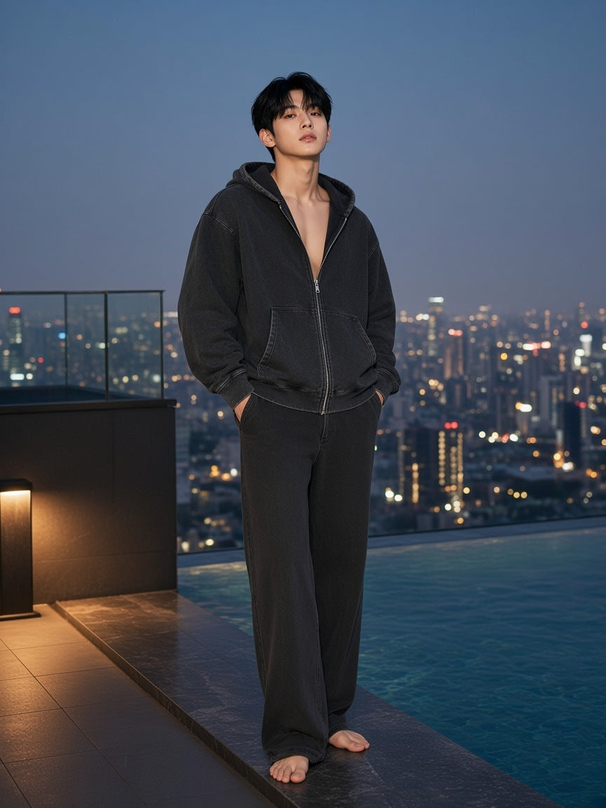 Marcel Afters Snow Wash Oversized Zip-Up Hoodie — Dark in Black, worn by a man, standing barefoot on a rooftop pool ledge above the city at dusk