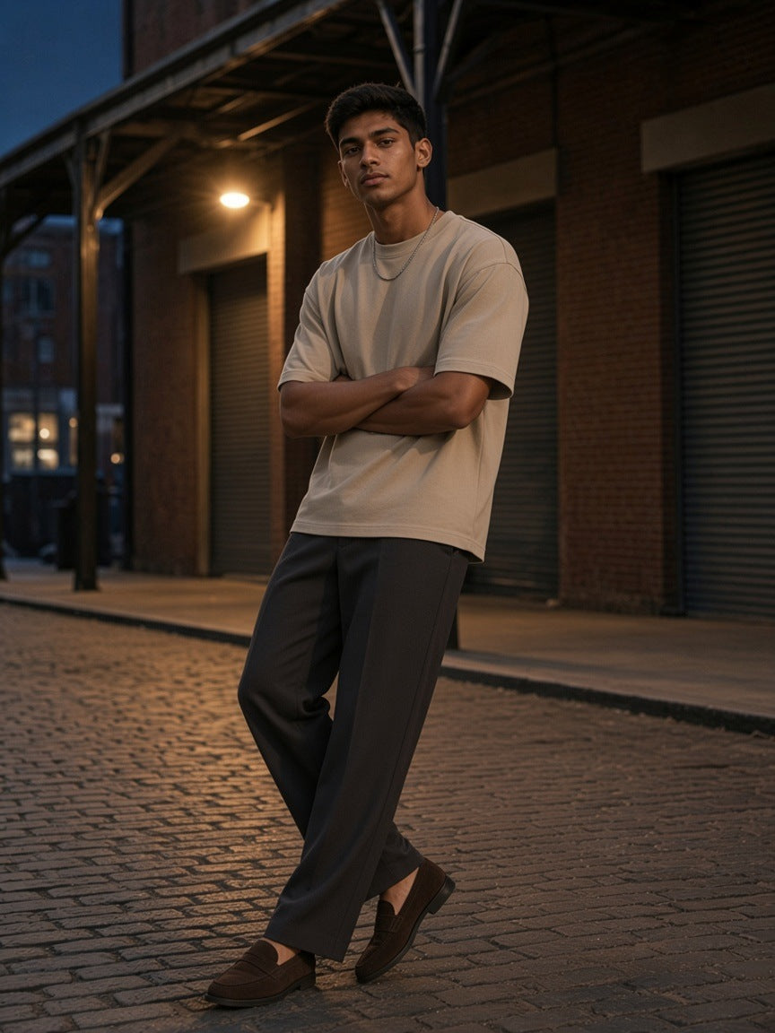 Man in a Khaki snow washed heavyweight oversize t-shirt leaning on a canopy post on a brick warehouse street at dusk