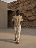 Marcel Afters Snow Washed Heavyweight Oversize T-Shirt in Khaki, worn by a man, walking a sandstone courtyard in cream trousers