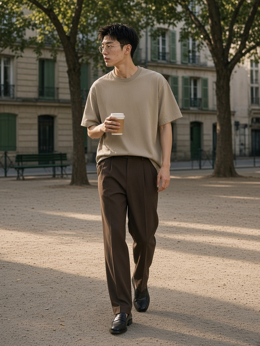 Man in the Snow Washed Heavyweight Oversize T-Shirt in Khaki walking with a coffee through Place Dauphine in Paris