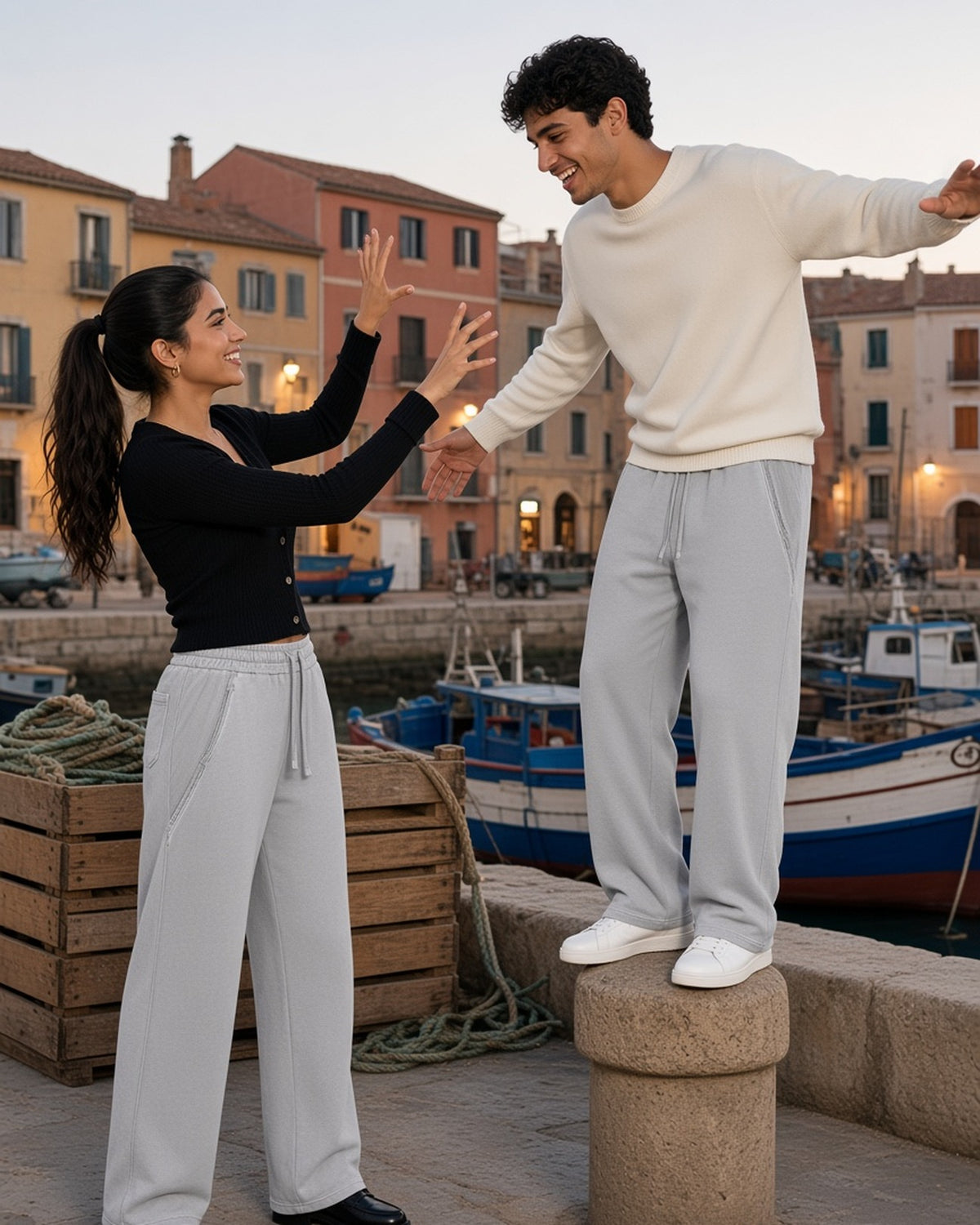 Two people in the Snow Washed Tape Raw Edge Sweatpants in Light Gray, clowning on a harbour bollard at dusk