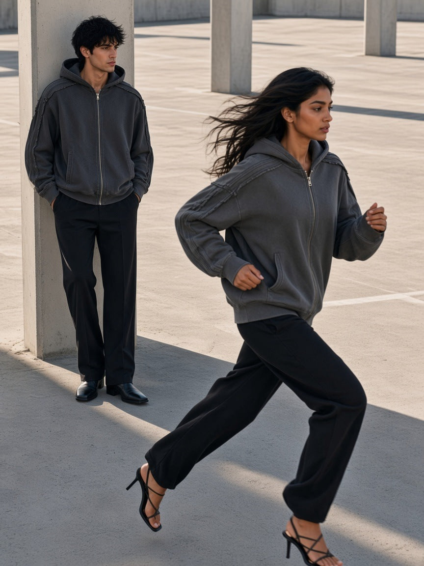 Two people in the Snow Washed Tape Raw Edge Zip Hoodie in Dark Gray, a woman running in heels across a concrete deck, a man leaning on a column behind, Los Angeles