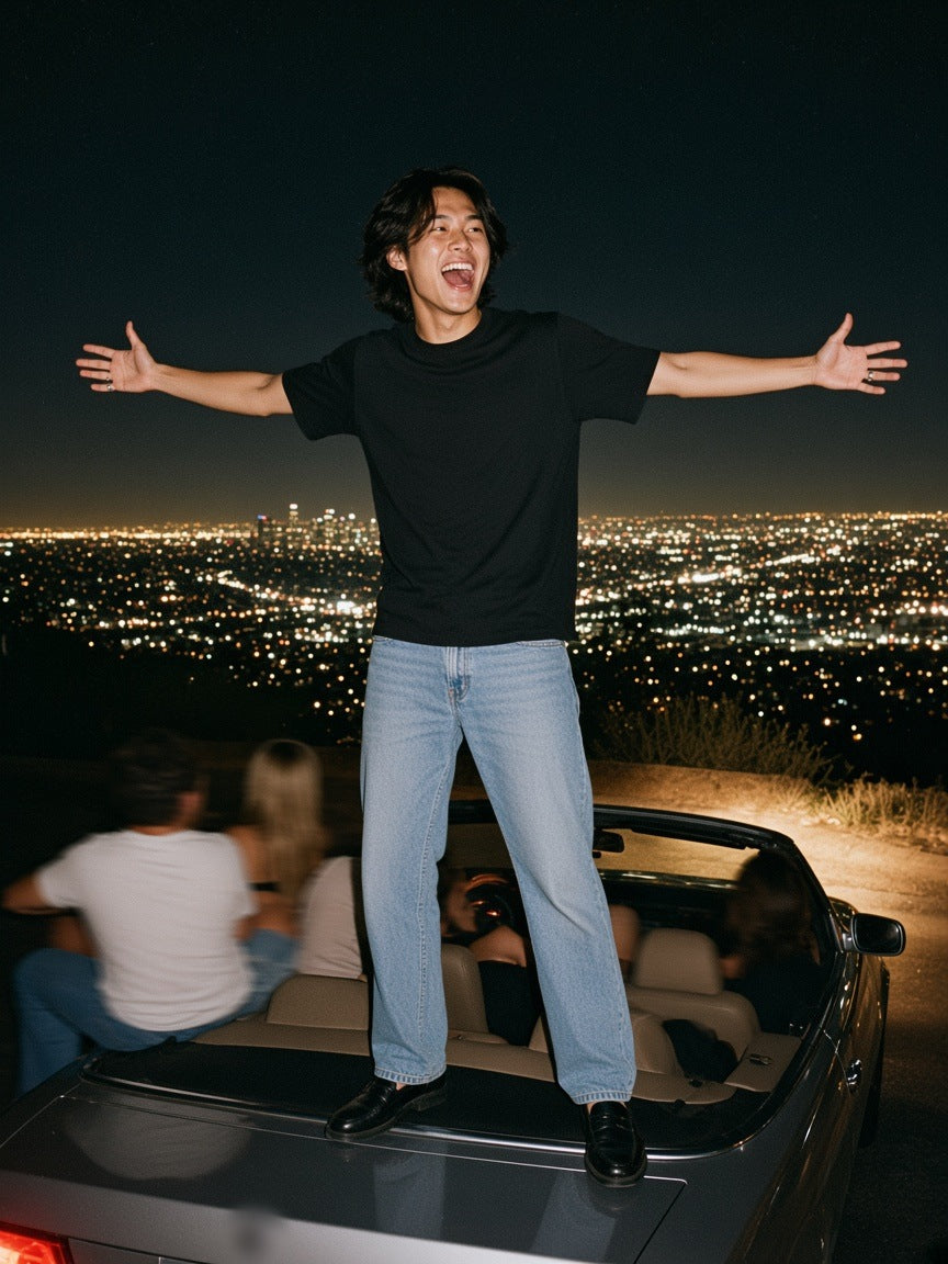 Man in the Solid Color Regular Fit T-Shirt in Black, standing on a convertible above the Los Angeles lights at 2am