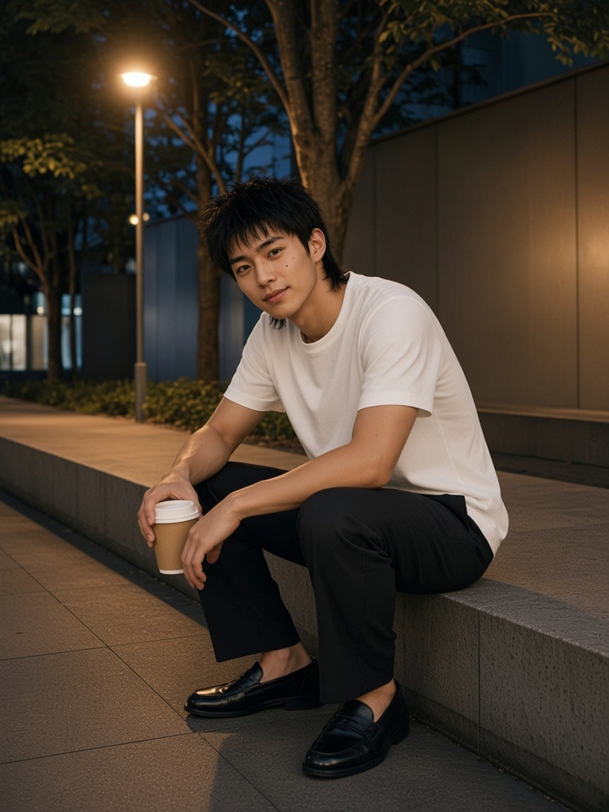 Man in the Solid Color Regular Fit T-Shirt in White with charcoal trousers and penny loafers, sitting on a planter ledge on an empty Tokyo avenue at 3am with a coffee