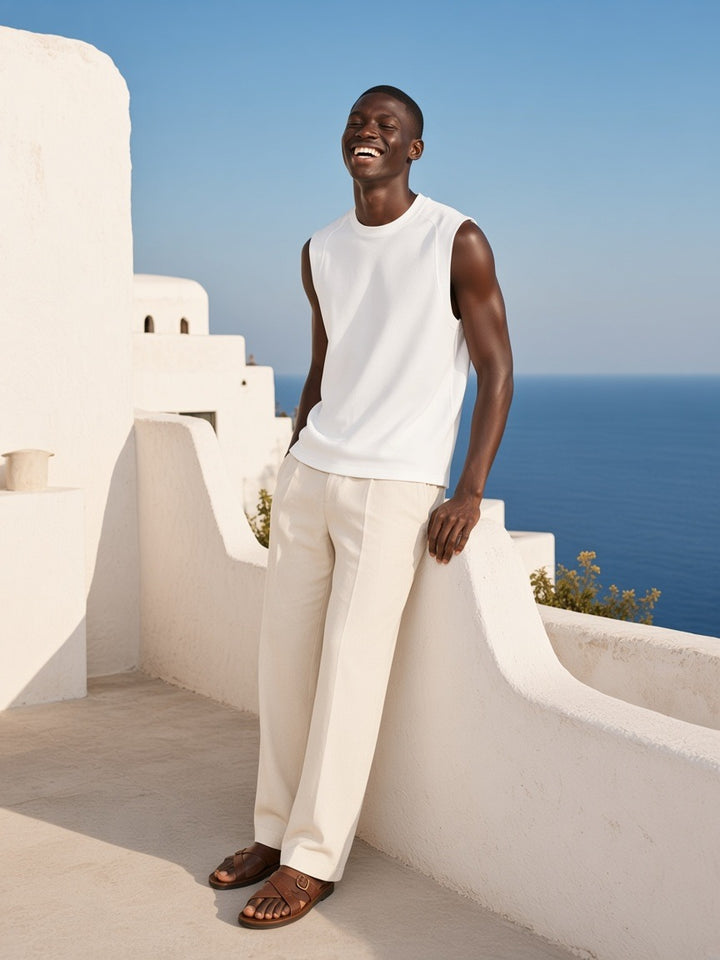 Marcel Afters Sorona Quick-Dry Cooling Tank Top in White, worn by a man, leaning on a whitewashed terrace wall above the sea