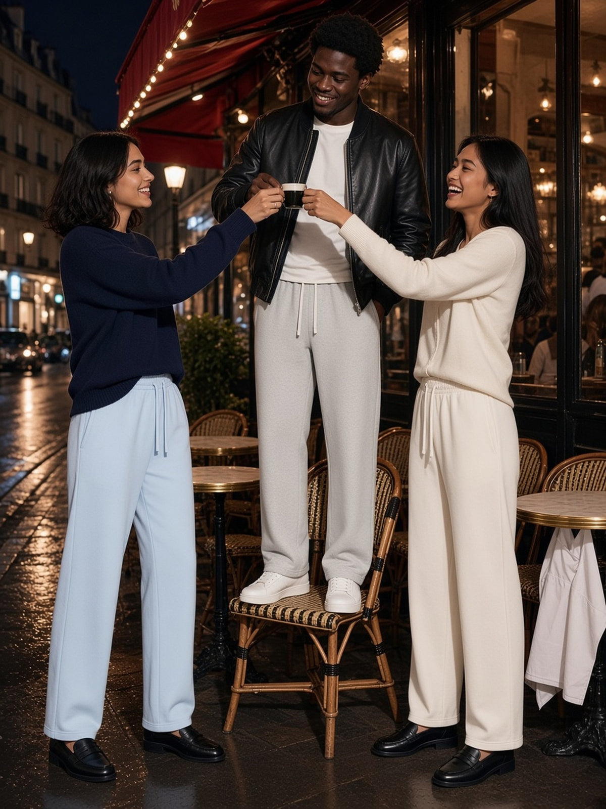 Three people in the Straight Leg Sweatpants in Sky Blue, Oat Gray and White, toasting on a Paris café terrace at night