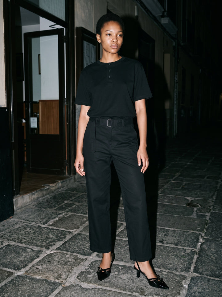 Woman wearing The After Six Slingback in Black with black belted barrel-leg cotton chino trousers and a black short-sleeve henley, flash photograph