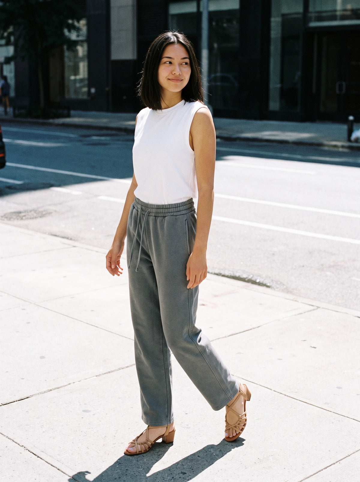 Woman wearing The Beach Club Sandal in Almond with medium gray vintage-washed straight-leg wide-waist trousers and a white tank top, flash photograph