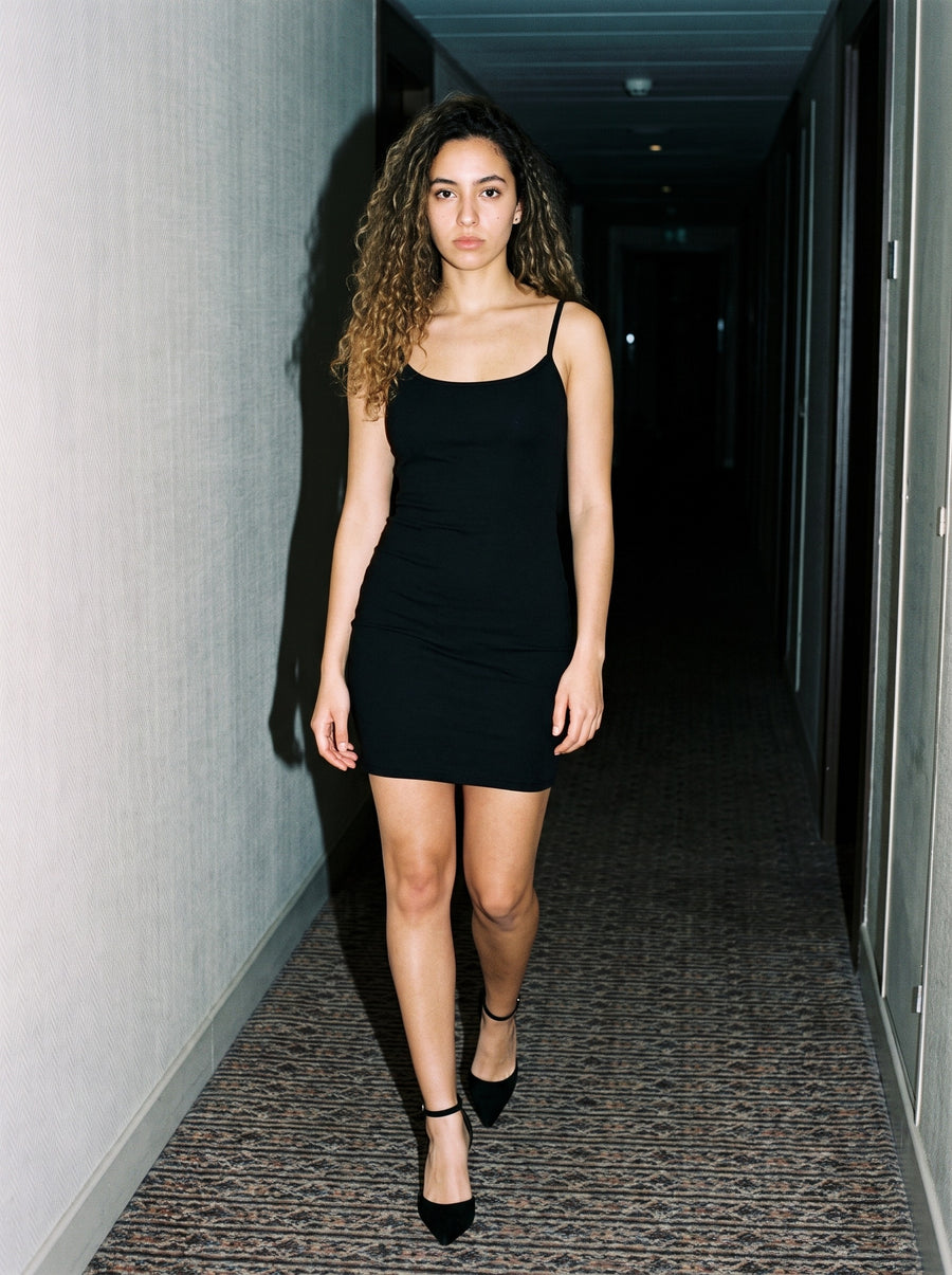 Woman wearing The Black Tie Pump in Black with black fine-strap close-fitting mini dress, flash photograph