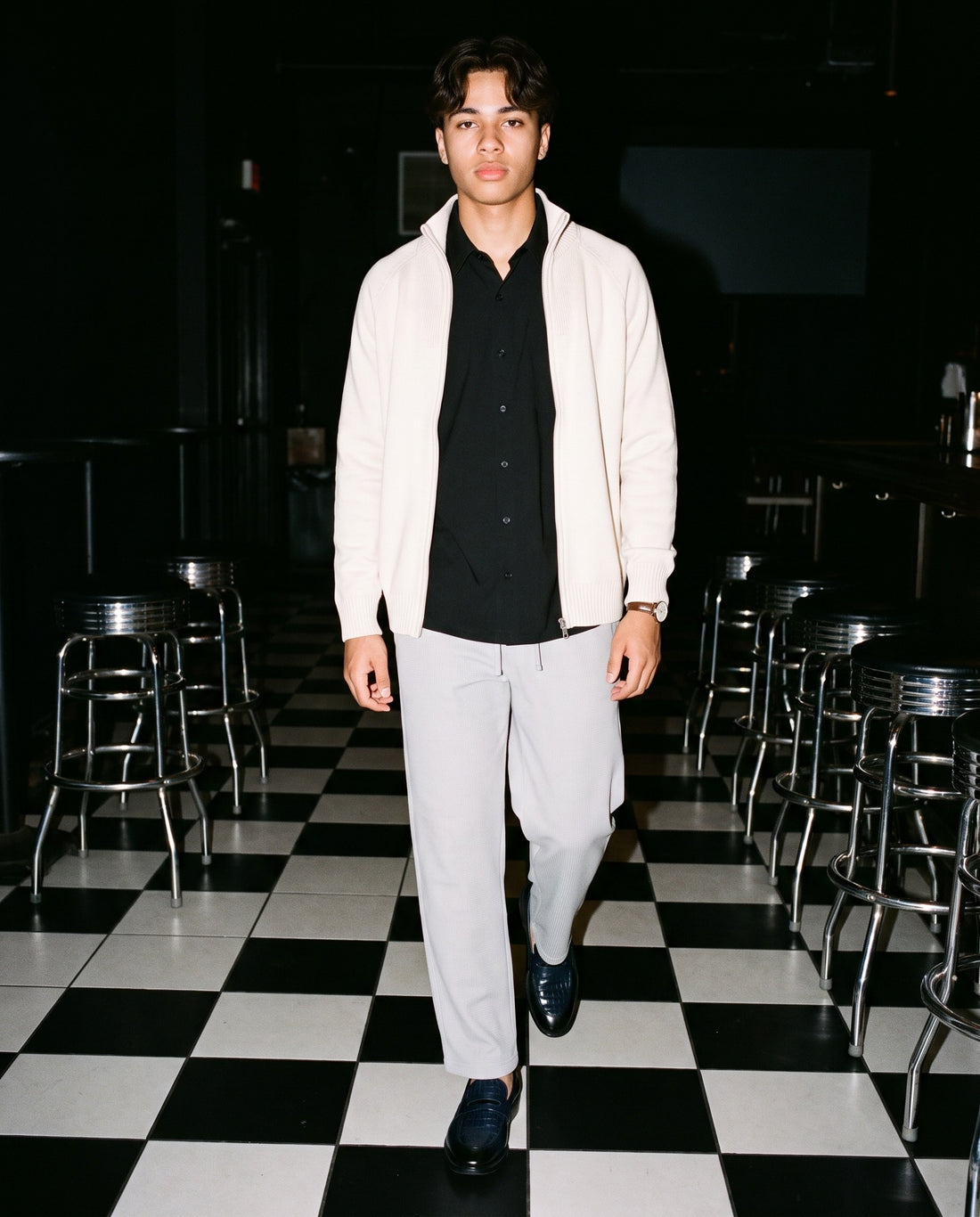 Man in Marcel Afters The Blue Room Loafer in navy, walking across a black and white checkerboard floor at night