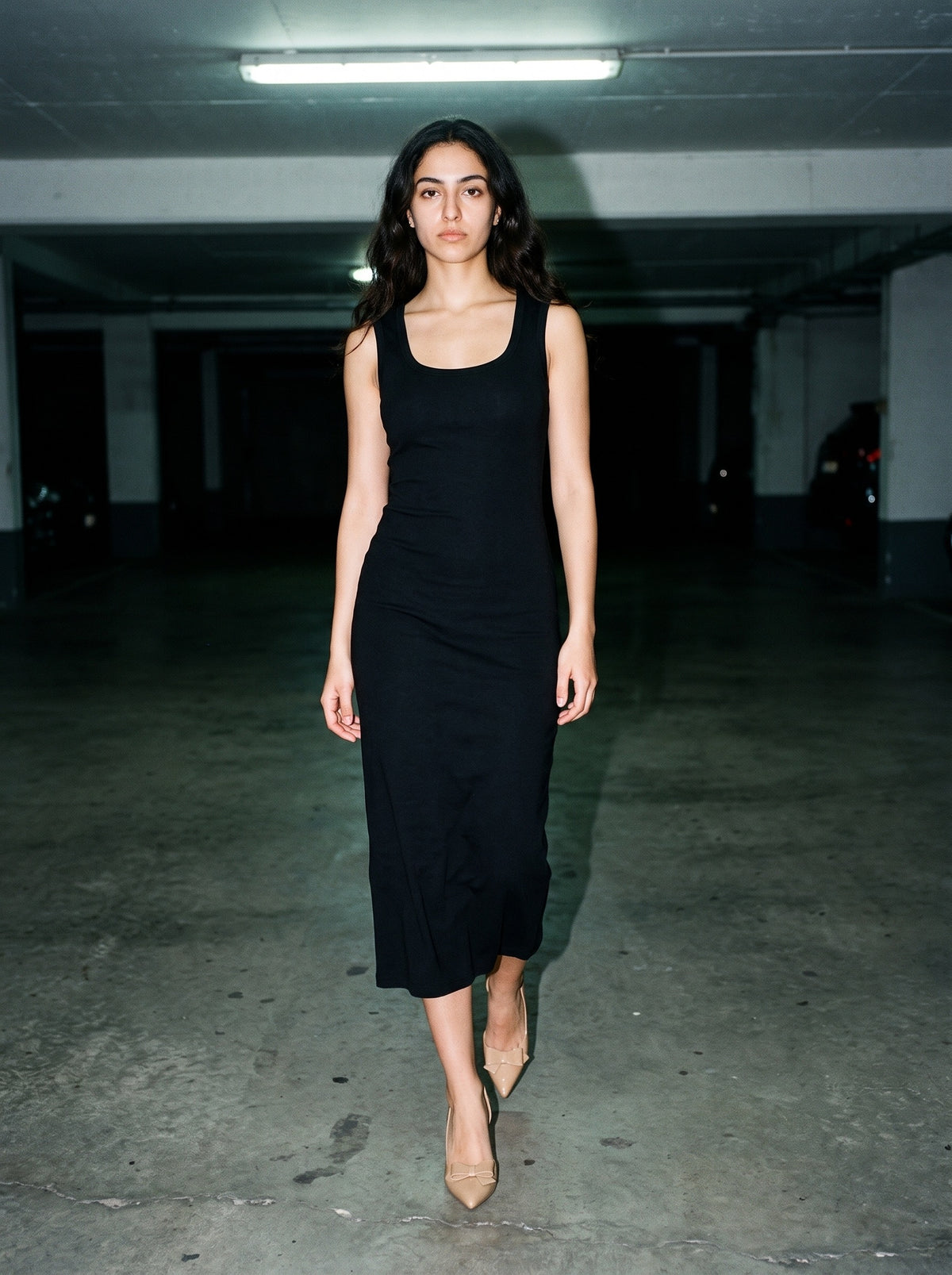 Woman wearing The Curtsy Pump in Nude with black scoop-neck sleeveless calf-length slim knit dress, flash photograph