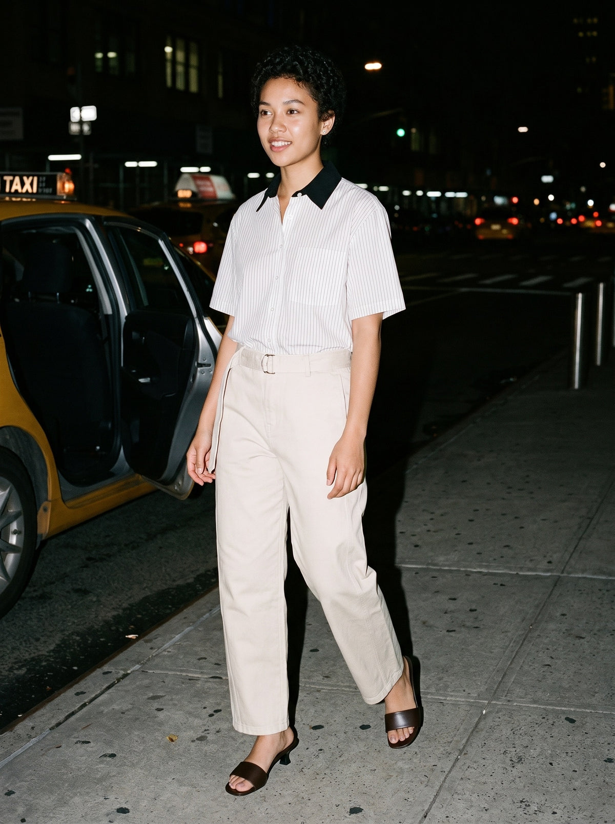 Woman wearing The Espresso Martini Mule in Dark Brown with beige belted barrel-leg cotton chino trousers and a white striped boxy shirt with contrast collar, flash photograph