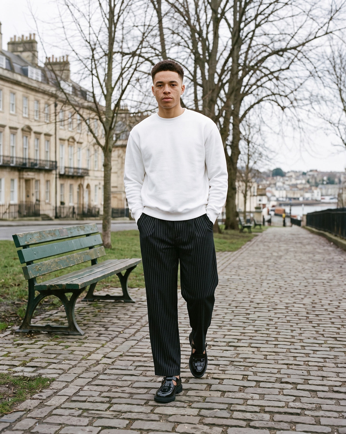 Man wearing The Harbour Bar Monk with the Heavyweight Crewneck Sweatshirt in White, Striped Pleated Pants in Black. Weekend Uniform, Autumn–Winter 2026 campaign