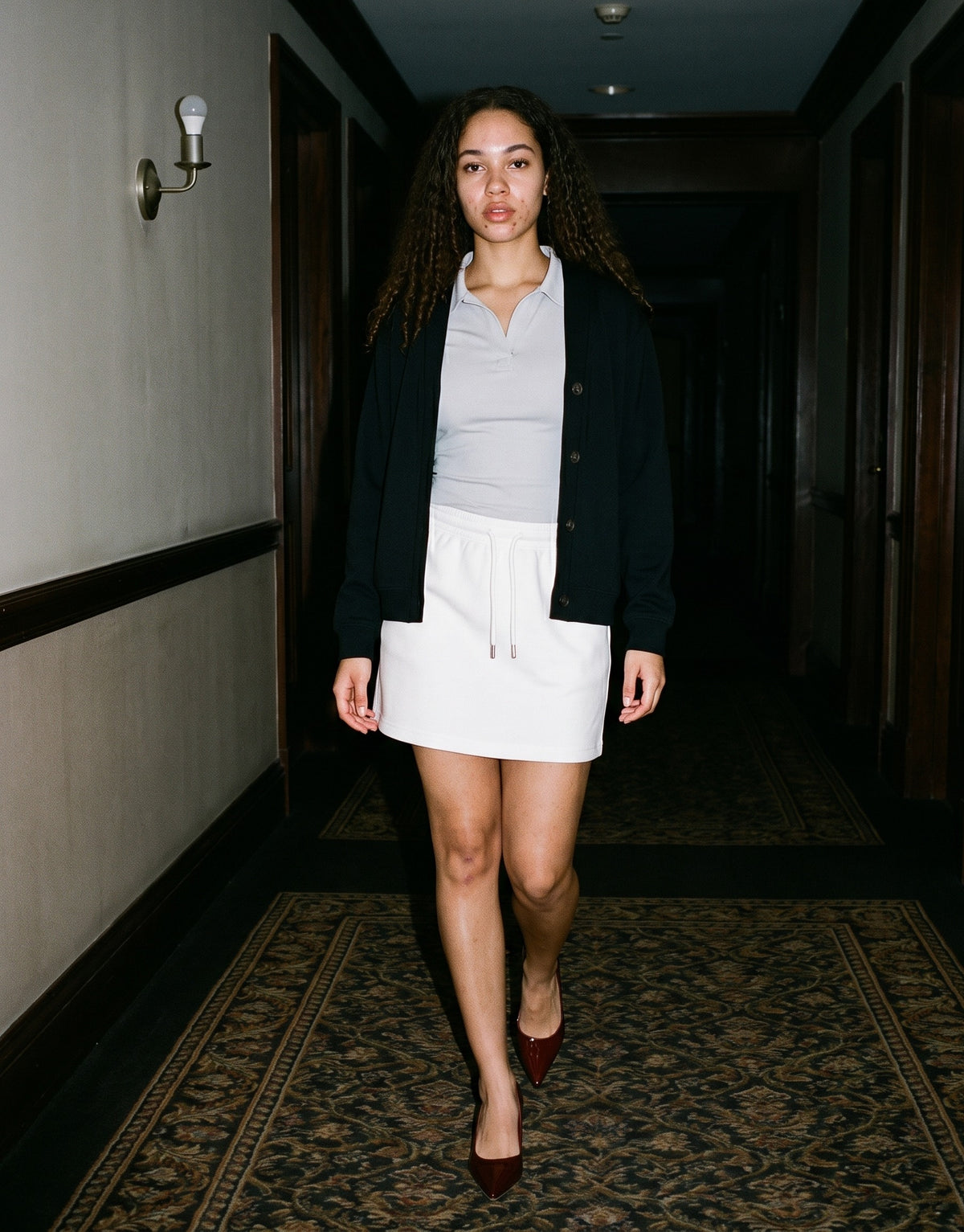 Woman wearing The Last Word Pump with the Bodycon Short Sleeve Polo Shirt in Gray, Essential Drawstring Skirt in White, Essential Heavyweight Sweat Cardigan in Black. Past Midnight, Autumn–Winter 2026 campaign