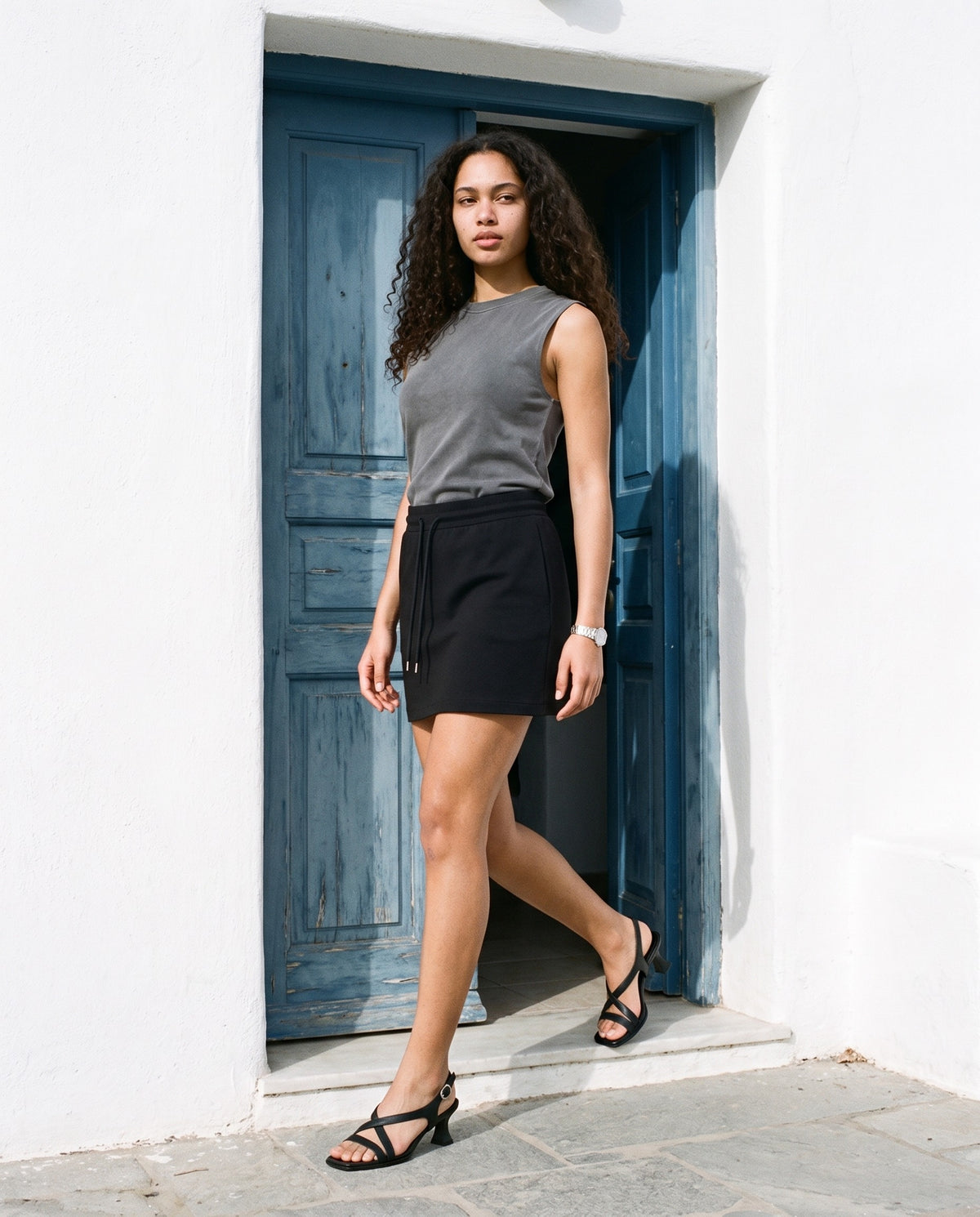 Woman wearing The Late Lunch Sandal with the Reverse Washed Tank Top in Gray, Essential Drawstring Skirt in Black. Travel Light, Autumn–Winter 2026 campaign