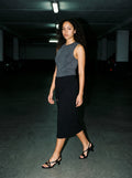 Woman wearing The Late Lunch Sandal in Black with black midi drawstring-waist jersey skirt and a gray tank top, flash photograph