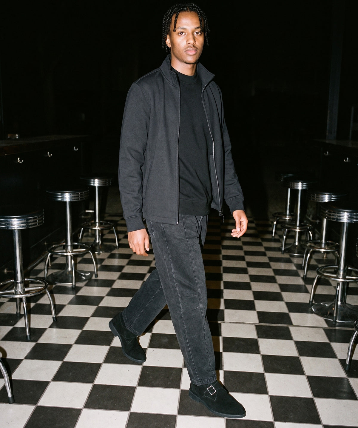 Man wearing The Late Table Monk with the Mock Neck Sweatshirt in Black, Mineral Wash Barrel Leg Pants in Black, Stand Collar Jacket in Black. After Dark, Autumn–Winter 2026 campaign