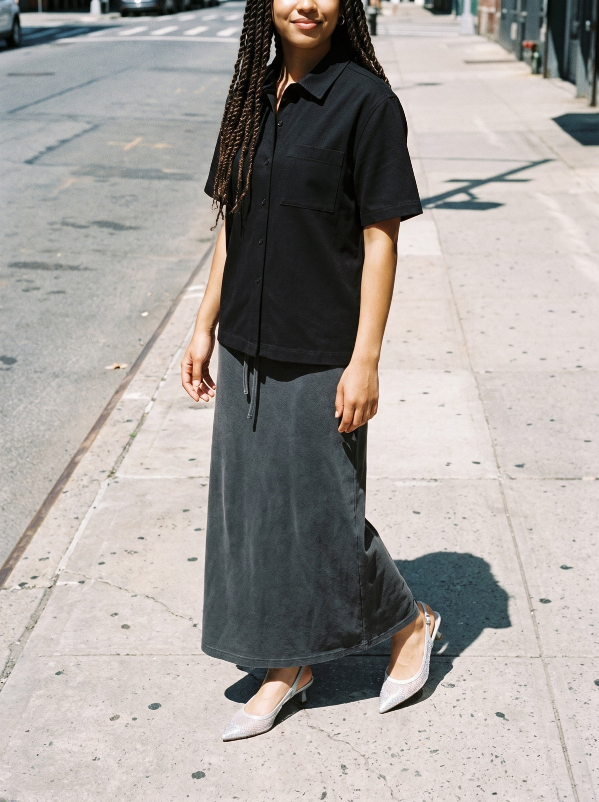 Woman wearing The Moonlight Slingback in Silver with dark gray washed ankle-length drawstring maxi skirt and a black boxy patch-pocket short-sleeve shirt, flash photograph