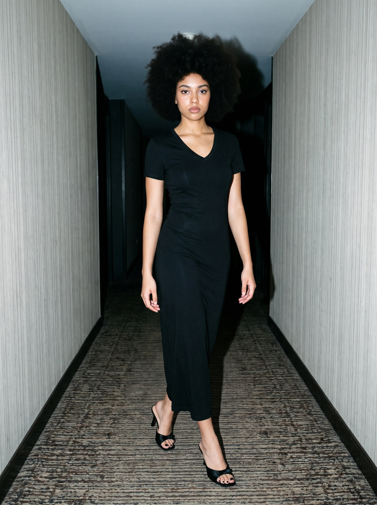 Woman wearing The Nightingale Mule in Black with black fitted V-neck short-sleeve ankle-length dress, flash photograph