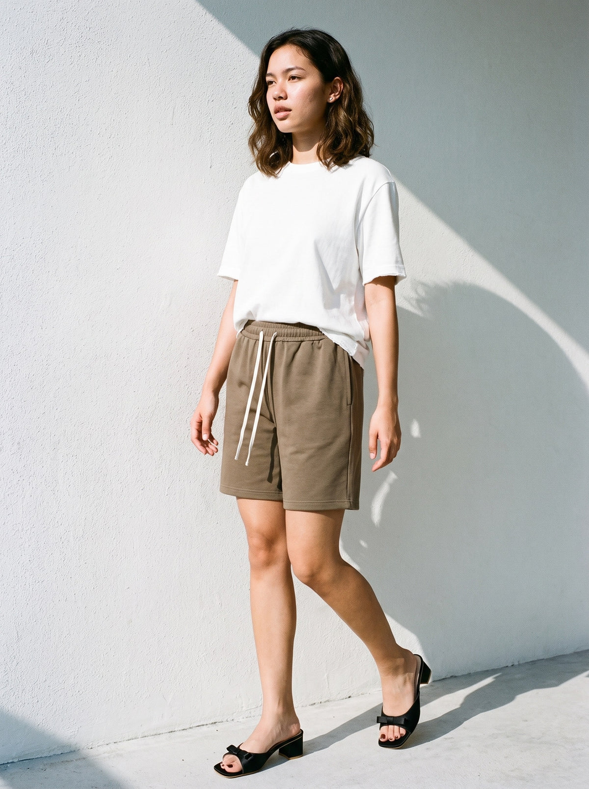 Woman wearing The Pillow Talk Mule in Black with coffee drawstring shorts and a white vintage-washed frayed tee, flash photograph