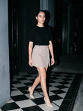 Woman wearing The Reservation Pump in Nude with light coffee high-waisted A-line knee-length skirt with pockets and a black short-sleeve knit henley tee, flash photograph