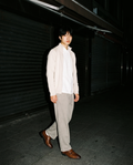 Man in The Second Bottle Monk in Brown with oat trousers and a cream knit jacket, walking a shuttered street at night