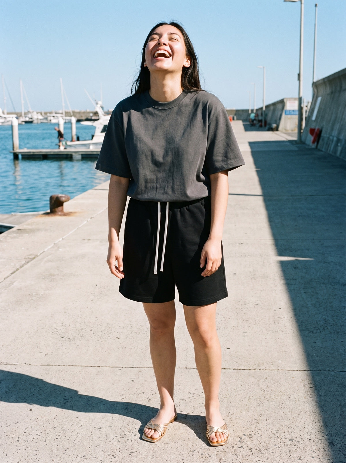 Woman wearing The Siesta Slide in Gold with black relaxed cotton shorts and a dark gray heavyweight drop-shoulder tee, flash photograph