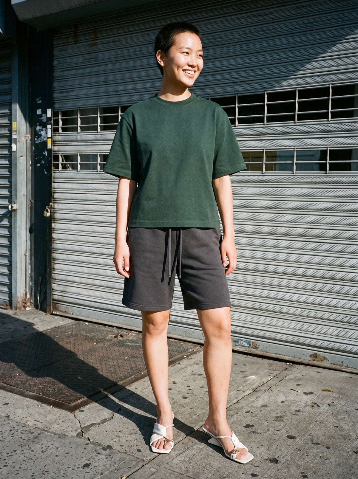 Woman wearing The Sun Deck Slide in Cream with charcoal gray heavyweight fleece sweat shorts and a black heavyweight boxy tee, flash photograph
