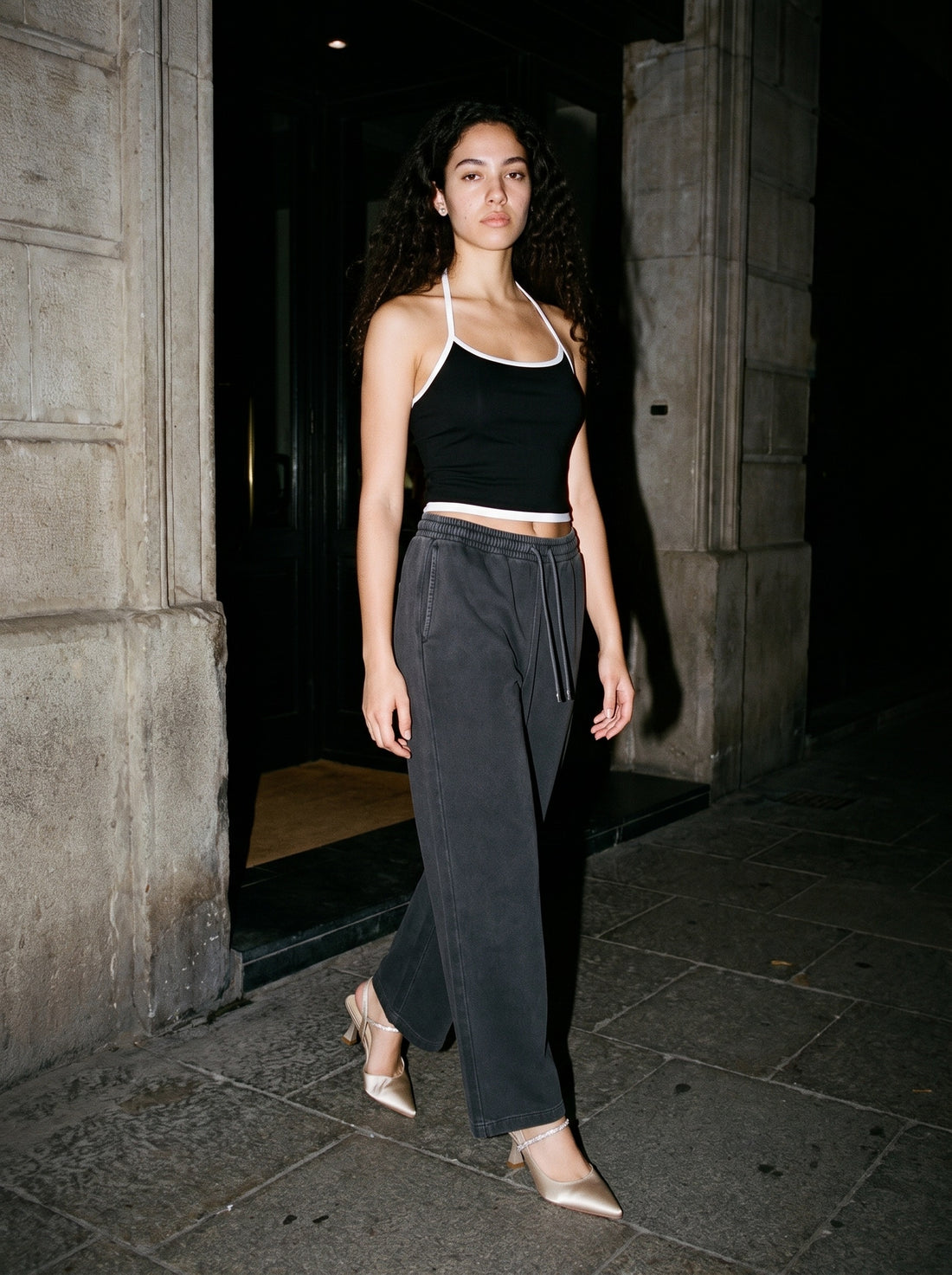 Woman wearing The Toast Slingback in Champagne with washed black straight-leg wide-waist trousers and a black halter top with contrast binding, flash photograph