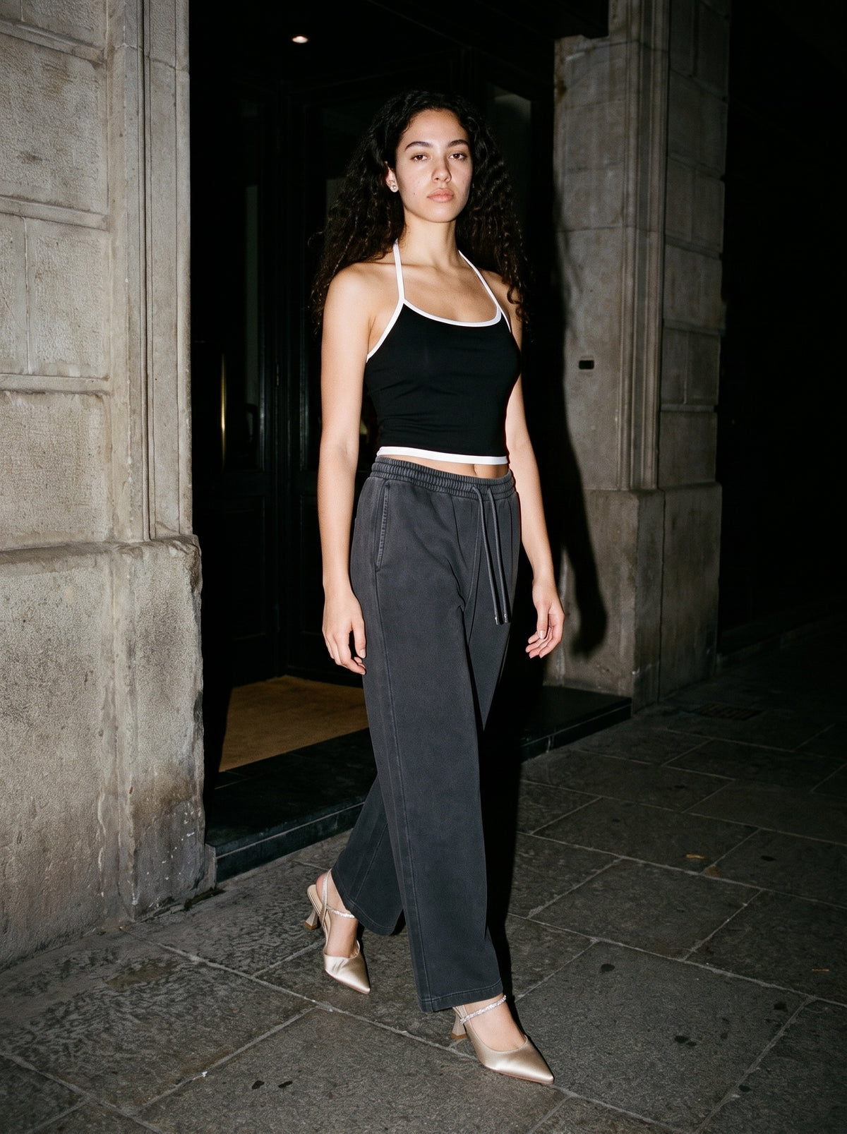 Woman wearing The Toast Slingback in Champagne with washed black straight-leg wide-waist trousers and a black halter top with contrast binding, flash photograph