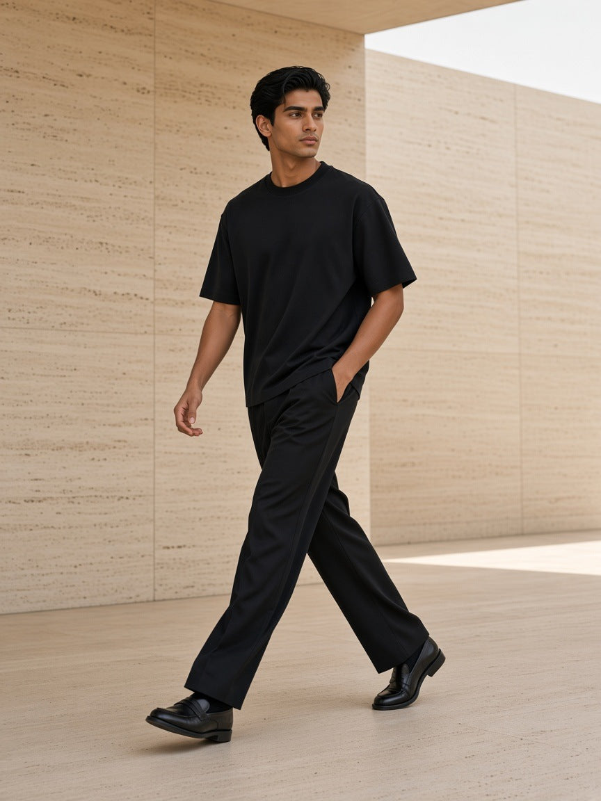 Marcel Afters Boxy Drop Shoulder T-Shirt in Black, worn by a man, walking through a travertine courtyard in black