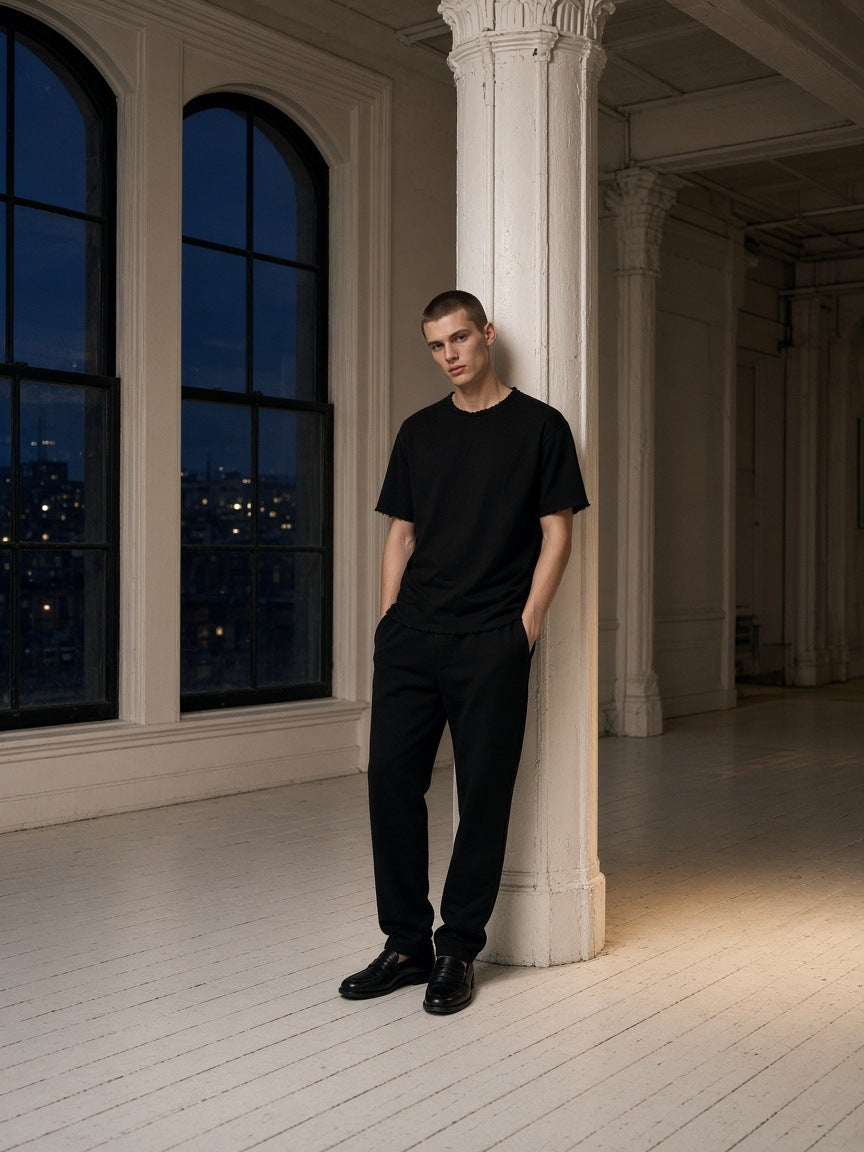 Marcel Afters Boxy Raw Edge T-Shirt in Black, worn by a man, leaning against a column beside arched windows