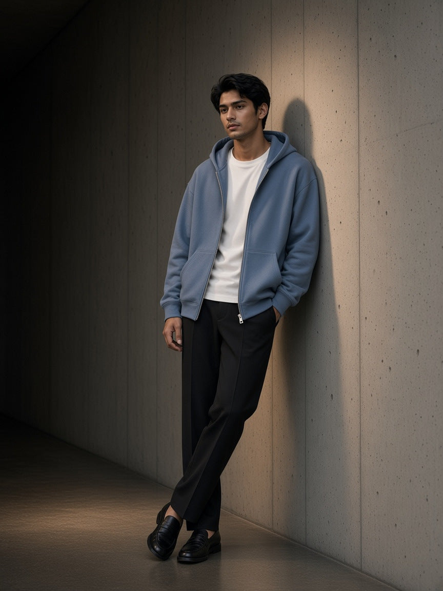 Marcel Afters Drop Shoulder Full Zip Hoodie in Haze Blue, worn by a man, leaning against a concrete wall in low light