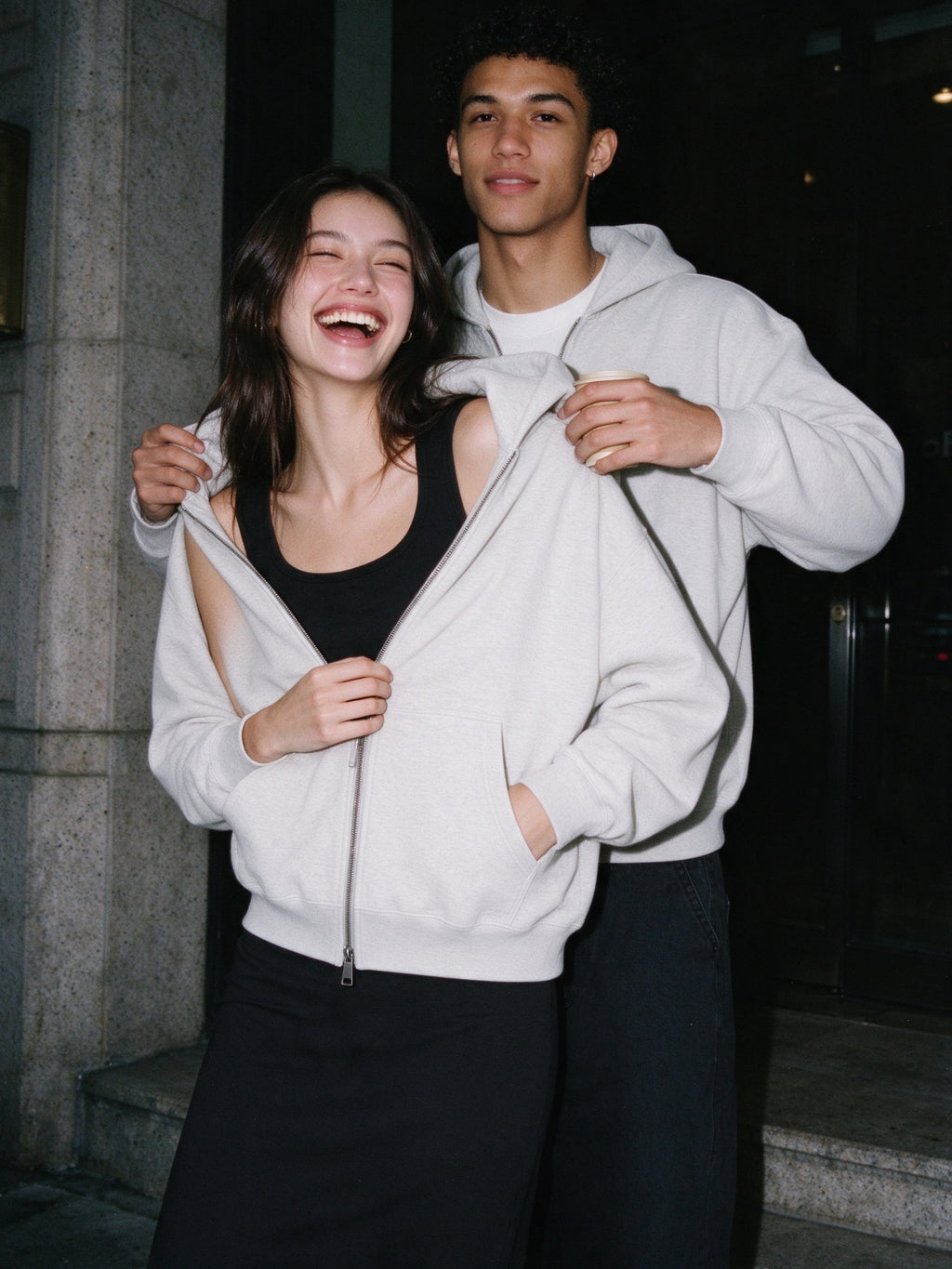 Woman wearing the Marcel Afters Heavyweight Full Zip Hoodie, Light Tones in Oat Gray, full-length editorial photograph