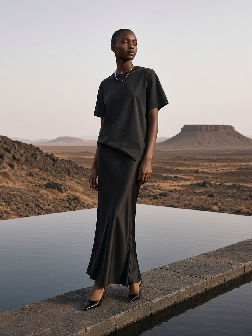 Marcel Afters Mineral Wash Oversized T-Shirt in Black, worn by a woman, standing on a stone ledge above a desert lake in a satin skirt