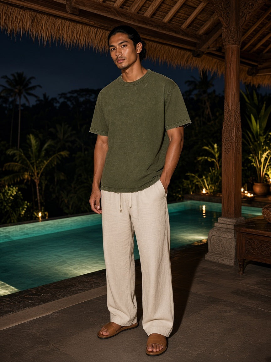 Marcel Afters Mineral Wash Oversized T-Shirt in Olive Green, worn by a man, standing barefoot by a lantern-lit pool at night