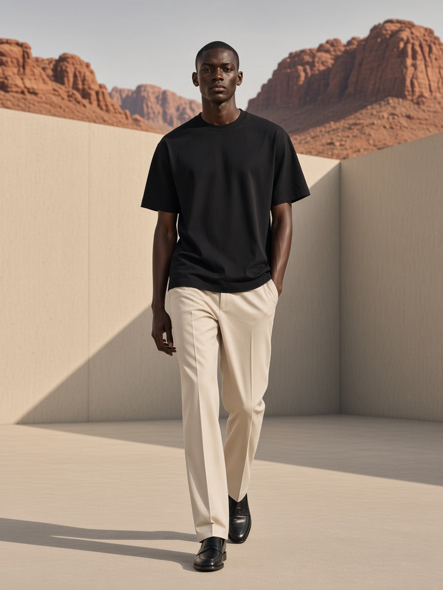 Marcel Afters Oversized Cotton T-Shirt in Black, worn by a man, walking a sunlit courtyard below red desert rock