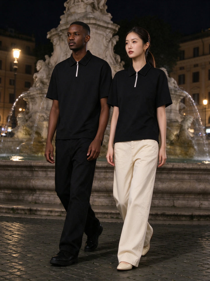 Marcel Afters Quarter-Zip Polo Shirt — Dark in Black, worn by a man and a woman, walking a night piazza past a stone fountain, he in a black quarter-zip polo and she in black